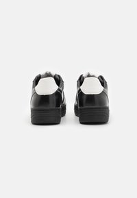 Sneaker in bianco e nero con tomaia in pelle liscia, colletto imbottito e suola in gomma spessa. Design minimalistico con colori a contrasto.