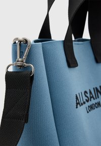Torba tote z płótna w jasnoniebieskim kolorze z czarnymi akcentami. Wyposażona w srebrny metalowy zamek i nadrukowane logo. Teksturowany materiał o sztywnym kształcie.