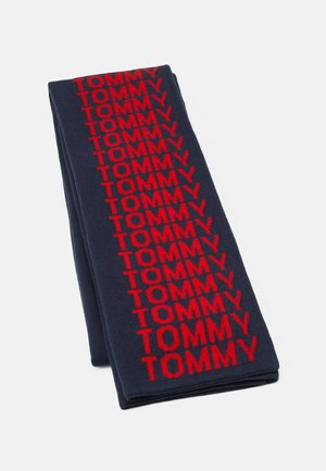 Złożony granatowy szalik z pionowo powtarzającym się napisem „TOMMY” w grubych czerwonych literach.