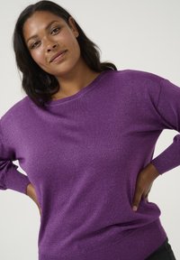 Purple knit sweater with a soft, sparkly texture; features a wide neckline and long sleeves, complemented by a snug ribbed waistband.