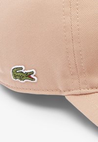 Casquette rose en tissu texturé avec une visière courbée, arborant un logo de crocodile vert brodé sur le côté.