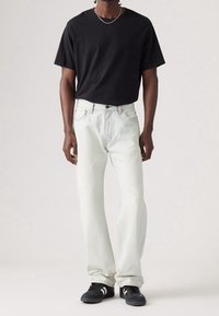 Czarny t-shirt z krótkim rękawem połączony z jasnoniebieskimi spodniami typu straight-leg i czarnymi trampkami z białymi paskami. Srebrny naszyjnik z łańcuszka dodaje detalu.