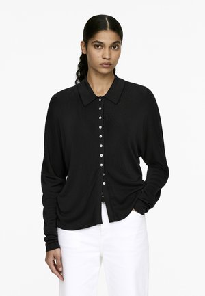 Black button-up shirt with a collar, made of a textured fabric, features long sleeves and a straight fit, with white buttons down the front.