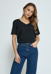 Camiseta negra de cuello en V en tejido suave, combinada con pantalones de denim azul de cintura alta que cuentan con una hebilla de cinturón circular dorada y corte de pierna ancha.