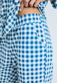 Conjunto de pijama em tecido quadriculado azul e branco com um cós elástico, apresentando um detalhe de costura desfiada do lado esquerdo das calças.