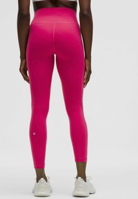 Roze high-waisted leggings met een gladde textuur, een strak aansluitend ontwerp en een klein logo detail nabij de enkel, gecombineerd met witte sportschoenen.