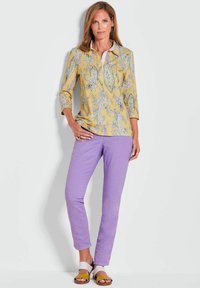 Geel paisley blouse met driekwartmouwen, gecombineerd met lavendel broek en sandalen met gele, witte en bruine accenten.