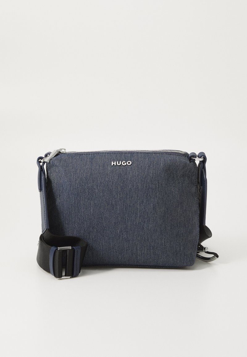 Denim crossover veske i mørkeblått med HUGO-logo, glidelås, justerbar svart stropp og slankt rektangulært design. Holdbart stoff.
