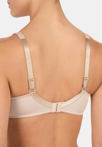 Soutien-gorge beige avec bretelles réglables, texture lisse, et un fermoir à crochets au dos. Design simple sans embellissements visibles.