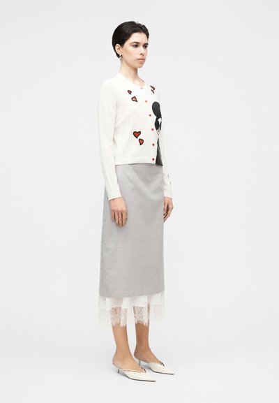 Fehér kardigán fekete és piros szívmintákkal, szürke szoknyával, csipkés szegéllyel. Vékony, testhez simuló szabás; hegyes fehér cipők.