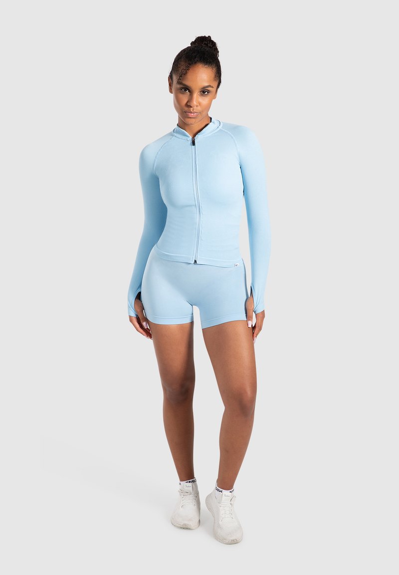 Maglia atletica azzurro chiaro con zip, maniche lunghe e pantaloni corti abbinati, realizzata in tessuto elasticizzato; design aderente, texture liscia e decorazioni minime.