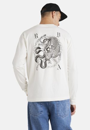 Long-sleeve cream shirt featuring a black graphic of a leopard and an octopus, surrounded by chain patterns, on the back. Cotton material.