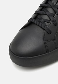 Sneaker in pelle nera con punta tonda, suola piatta in gomma e lacci neri testurizzati. Presenta cuciture minime e una finitura liscia.