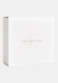 Boîte en carton blanc avec une finition lisse, présentant un logo en relief subtil "Calvin Klein Jeans" en or sur le devant.