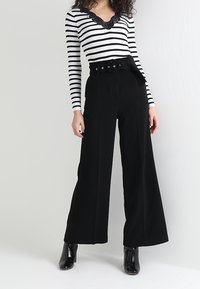 Pantalon noir taille haute à jambes larges avec une ceinture à la taille, assorti à un haut à manches longues rayé noir et blanc avec un col en dentelle.
