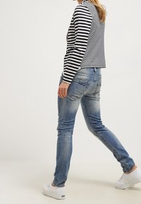 Maglietta a maniche lunghe a righe abbinata a jeans in denim azzurro chiaro. I jeans presentano una texture sbiadita e lievi strappi, completati da sneakers bianche.