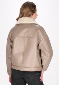 Giacca in pelle beige con colletto in pelliccia bianca morbida, vestibilità rilassata e dettagli di cucitura sottili, abbinata a jeans scuri.