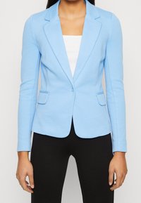 Jasnoniebieska marynarka z wyciętym kołnierzem, pojedynczym zapięciem na guzik i dwoma kieszeniami z przodu, wykonana z gładkiej, elastycznej tkaniny.