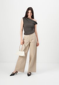 Gray one-shoulder top with gathered texture, paired with beige wide-legged pants. Model holds a cream handbag and wears black pointed shoes.