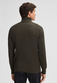 Olivengrüner, gerippter Rollkragenpullover mit langen Ärmeln. Besitzt ein tailliertes Design und ein dezentes strukturiertes Muster am Kragen und an den Bündchen.