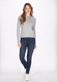 Šedý žebrovaný cardigan s kulatým výstřihem, zapínáním na knoflíky a dlouhými rukávy, v kombinaci s tmavě modrými skinny džíny a bílými teniskami.