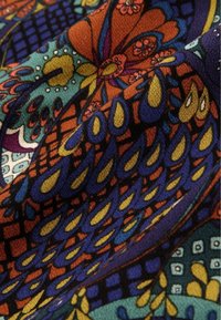 Färgglad tyg med detaljerade blommönster och droppmönster i orange, blått, gult, lila och teal, som visar struktur och veck.