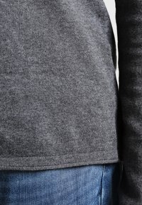 Szary dziany sweter z prążkowanym obszyciem. Miękka faktura, lekko luźny krój, zestawiony z niebieskimi dżinsami. Obecne subtelne detale szwów.