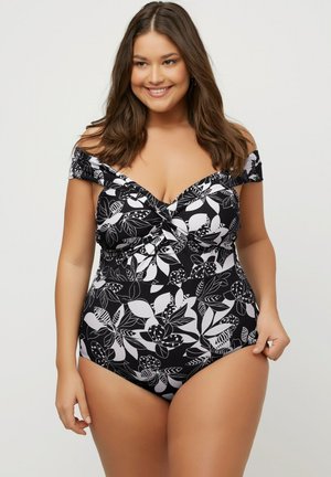 Maillot de bain une pièce noir avec un motif floral blanc, design décolleté, détail noué à l'avant et texture de tissu lisse.