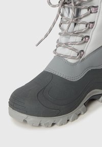 Bota impermeable de invierno con suela y puntera de goma gris, parte superior de tela gris claro y cordones redondos con patrón gris y rosa.