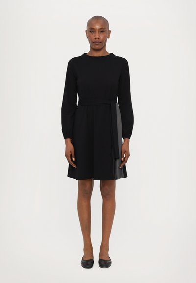 Abito lungo nero a maniche lunghe con bodice aderente, gonna svasata, dettaglio con piega laterale e cintura regolabile in vita. Realizzato in tessuto liscio.