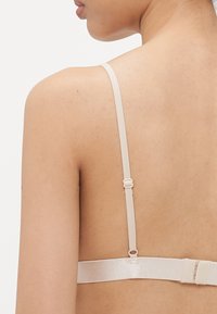 Beige bh met verstelbare bandjes, zachte textuur, haak-en-oogsluiting aan de achterkant en een minimalistisch ontwerp.