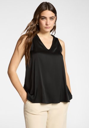 Sort ærmeløs bluse med V-udskæring. Fremstillet af glat, satinlignende stof. Løs pasform, sidelommer, kombineret med beige bukser.
