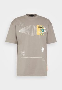 Harmaa puuvillapaita rennoilla leikkauksilla, jossa on valkoisia graafisia viivoja, keltainen logo-patch ja rohkeita muotoiluelementtejä edessä.