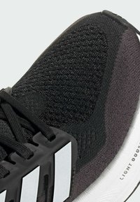 Svart sportskor med texturerad svart ovandel, framträdande vita sidodetaljer och en rundad vit sula märkt "LIGHT BOOST."