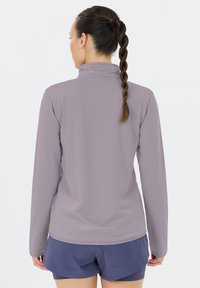 Sportieve lange mouwen top in zachte lavendelstof, met een hoge kraag, een getailleerd ontwerp en een gestructureerd patroon. Gecombineerd met donkere shorts.