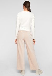 Haut blanc à manches longues associé à un pantalon large côtelé rose pâle, avec une surface texturée et une coupe décontractée. Des baskets de couleur claire complètent le look.