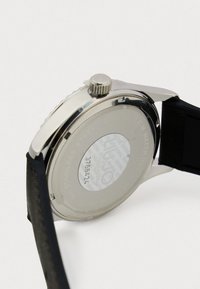 Edelstahl-Gehäuseboden mit glatter Oberfläche, gravierten Details, Schraubkrone und schwarzem Silikonarmband. Sichtbare Wasserresistenz-Markierungen.