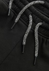 Zwarte sweatpants met een elastische tailleband. Verstelbare trekkoorden in een gevlochten grijze uitvoering, met glanzende plastic uiteinden. Zachte textuur.