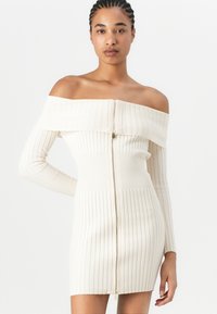 Offshoulder ribbestrikket kjole i kremfarge, med full frontglidelås, lange ermer og en tettsittende silhuett som går til midten av låret.