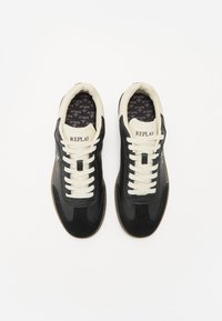 Des baskets noires avec un mélange de textures lisses et en daim, des lacets crème et une semelle en caoutchouc marron. Logo "REPLAY" affiché sur la languette.