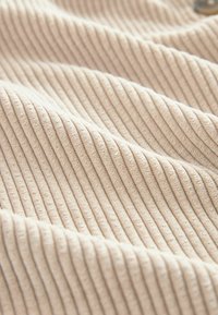 Beiger Rippstoff mit weicher Textur, der erhabene vertikale Streifen aufweist. Die Oberfläche wirkt leicht plüschig und gut verarbeitet.