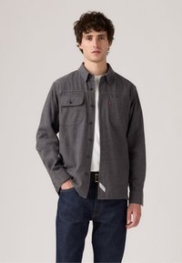 Grijze button-up shirt van gestructureerde stof, met twee borstzakken, een kraag en een label op de zoom, gecombineerd met donkere jeans.