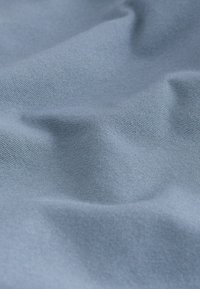 Lichtblauwe stof met een gladde textuur, voorzien van zachte plooien en fijne geweven patronen, wat wijst op een zachte en flexibele materiaalkwaliteit.