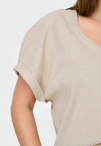 Beige ribbet striktop med korte opkrøllede ærmer og V-halsdesign. Stoffet har en subtil struktur, hvilket giver den et blødt udseende.