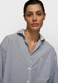 Chemise à rayures bleu marine et blanche avec boutonnière, dotée d'un col, d'une poche avant et d'une texture de tissu douce. Couture détaillée sur le col.