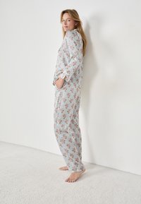 Pyjama set met bloemenpatroon en verticale strepen; zachte stof; lange mouwen; shirt met voorzakken; losse broek.