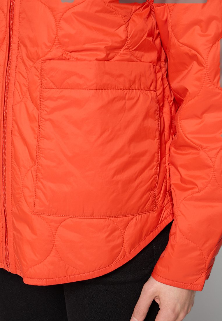 Kurtka pikowana w kolorze pomarańczowym, z zamkiem błyskawicznym, z boczną kieszenią i gładką teksturą. Krój z lekko zaokrąglonym dołem i luźniejszym fasonem.
