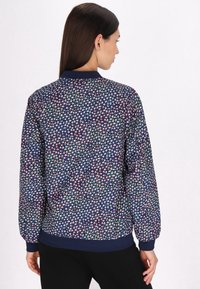 Jachetă de bombardieră bleumarin cu un model geometric multicolor, guler și mansete ribbed și o croială lejeră. Are o textură netedă și un tiv elastic.