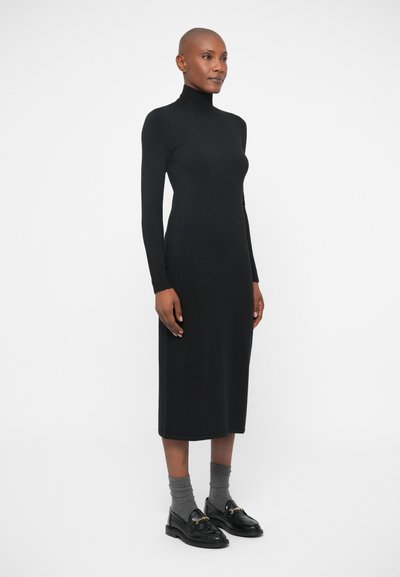 Melnas, pieguļošas midi kleitas ar augstu kaklu un garām piedurknēm. Apvienota ar pelēkiem zeķēm un melniem mokasīniem ar zelta akcentiem.