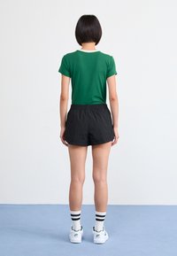 Žalias trumpomis rankovėmis marškinėliai su balta apykakle, derinami su juodais šortais. Baltos sneakers'ai su žaliais akcentais ir dryžuotos kojinės užbaigia aprangą.